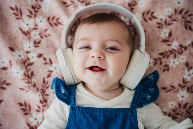 Creative Highlights Symbolbilder Cute baby girl wearing wireless headphones lying on bed model released, Symbolfoto property released, EBBF08796