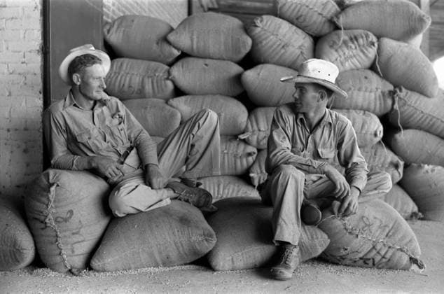 FARMERS, 1938. Two farmers sitting on burlap sacks of rice at a mill in Abbeville, Louisiana. Photograph by Russell Lee, September 1938.  Copyright: xGRANGERx xGRANGERx 0121659