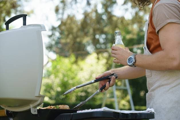 Man grilling on outdoor grill and drinkig lemonade. Outdoor grill or BBQ party in the garden. Man grilling on outdoor grill, holding tongs and drinkig lemonade. Outdoor grill or BBQ party in the garden. model released