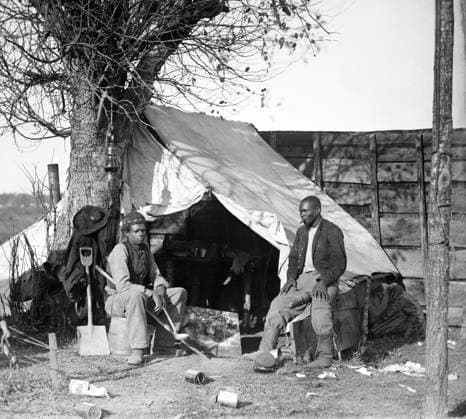 CIVIL WAR: CONTRABANDS. Two African American contrabands (freed slaves) sitting in front of a tent, one with cigar and the other with a soup ladle at a military cookery in Culpeper, Virginia. Photograph by Timothy O Sullivan, November 1863.  Copyright: xGRANGERx xGRANGERx 0163355