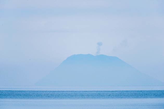 Creative Highlights World Am Horizont über dem Meer taucht der Stromboli mit seiner Rauchfahne aus dem Dunst. Vulkan Stromboli, Sizilien, Italien. Der Vulkan Stromboli am Horizont *** On the horizon above the sea, Stromboli emerges from the haze with its plume of smoke Stromboli volcano, Sicily, Italy Stromboli volcano on the horizon