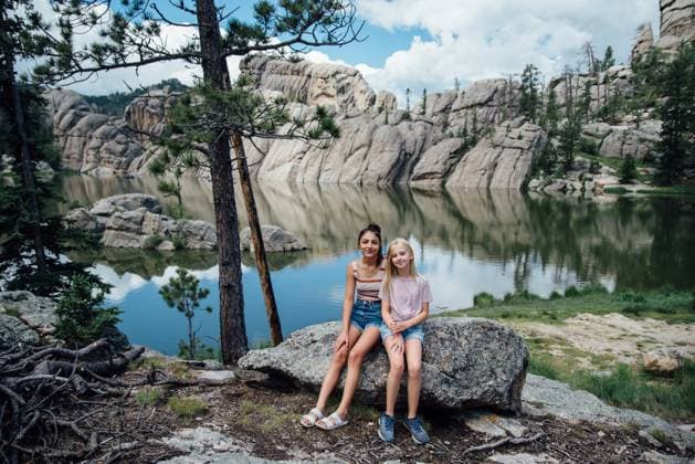 Creative Highlights Symbolbilder Portrait of two smiling teen girls sitting on rock in front of lake. Keystone, South Dakota, United States CR_KIFR240402-1377309-01 ,model released, Symbolfoto