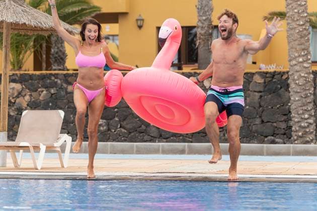 An ecstatic couple is captured in mid-motion, joyfully playing with a giant pink inflatable flamingo by a sunlit swimming pool Model Released JuanAizpuru_ID20330_601362_015 Copyright: xJuanxAizpurux