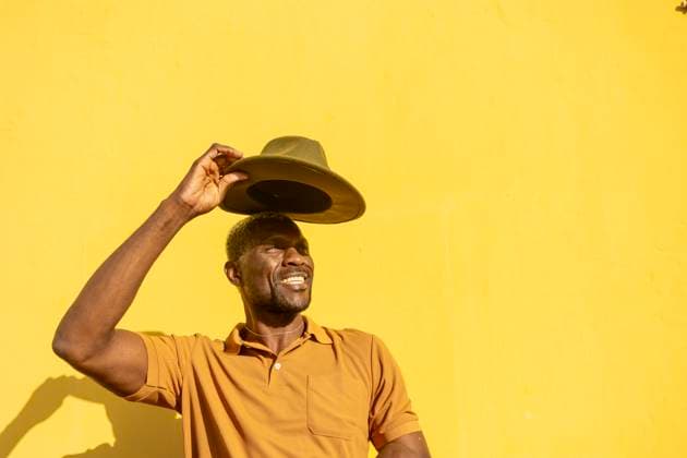 A cheerful African man tipping his hat with a sunny yellow background, evoking warmth and happiness Model Released JuanAizpuru_ID20348_601907_036 Copyright: xJuanxAizpurux