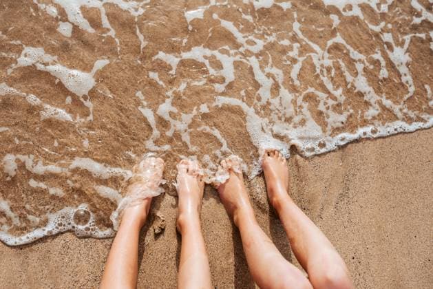 Close up of feet on beach with sea water beneath them. Sea foam and warm water soaking legs. Close up of feet on beach with sea water beneath. Sea foam and warm water soaking legs. model released