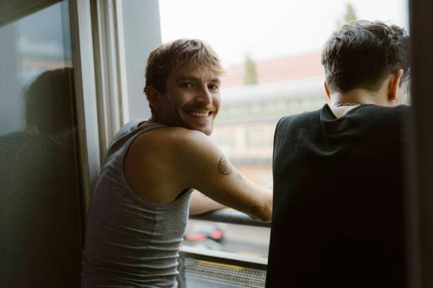 Creative Highlights Symbolbilder Smiling gay man looking over shoulder while standing with friend near window in apartment Germany, Berlin, model released, property released Copyright: xMaskotx , MA108370 MA108370
