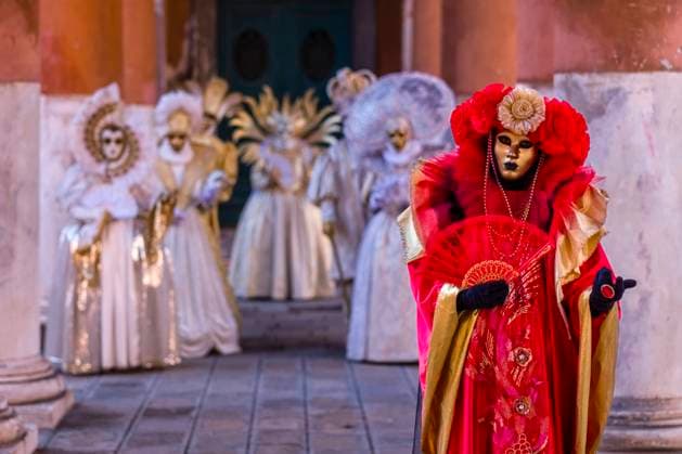 A group of masked persons in creative white and red costumes, posing between big pillars, celebrating the Venetian Carnival. Venice Veneto Italy FB_2024_0627