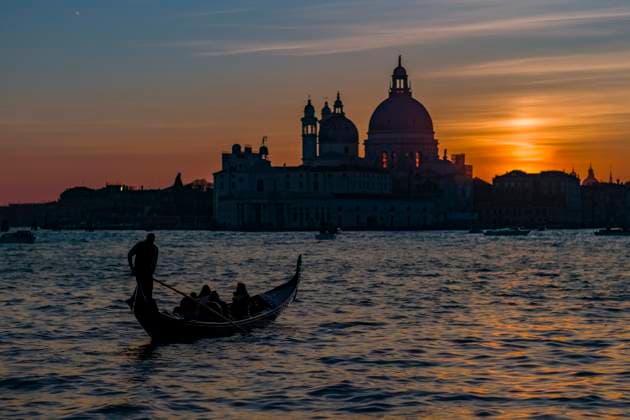 Basilica di Santa Maria della Salute at sunset, seen across the Canale della Giudecca, a gondola with tourists crossing the canal. Venice Veneto Italy FB_2024_0707