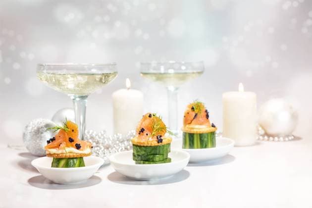 Festive canapes from smoked salmon, cucumber, crackers and caviar, in the background gasses with champagne, candles and decoration, holiday snack for Christmas or new year, copy space Festive canapes from smoked salmon, cucumber, crackers and caviar, in the background gasses with champagne, candles and decoration, holiday snack for Christmas or new year, copy space, selected focus Copyright: xZoonar.com MarenxWinterx 21130941