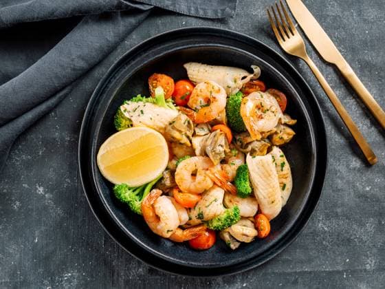 Salad with Mixed Seafood on dark plate Mixed Seafood Contain Shrimps, Mussels, Calamari Squids and Fish with Broccoli, Cherry Tomato, Lemon on Black dish in restaurant-style platting. Seafood salad on dark background. Top view Copyright: xZoonar.com OlgaxSergeevax 21172921