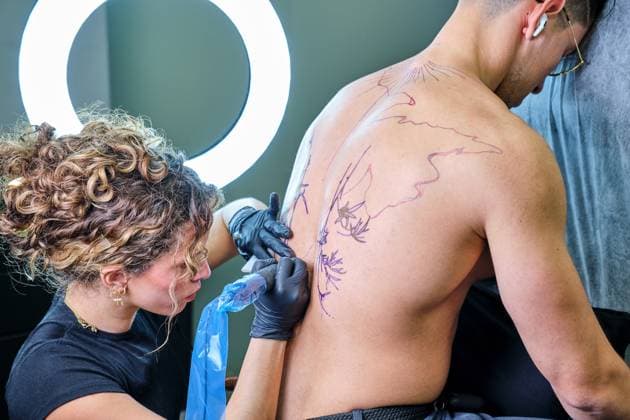 A focused female tattoo artist professionally inking a design on an unrecognizable client s skin in a well-equipped tattoo studio. Model Released Alvaromp_ID20429_604195_036 Copyright: xAlvarompx