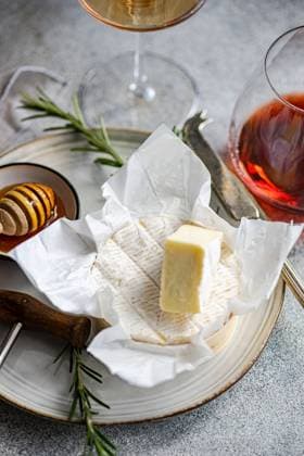 An elegant presentation of brie cheese with honeycomb, rosemary, and wine glasses on a textured surface for sophisticated dining. Model Released AnnaBogush_ID20594_608291_009 Copyright: xAnnaxBogushx