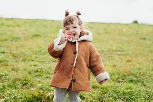 A cheerful young girl with cute buns smiling and playing in a field, wearing a warm brown coat Model Released HodeiUnzueta_ID20569_607691_010 Copyright: xHodeixUnzuetax