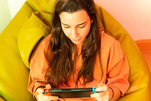 IMAGO Creative, Lifestyle, Gaming A focused gamer sits comfortably, deeply immersed in playing a game on a handheld console, with a vibrant yellow chair adding a pop of color Model Released NataliaPenado_ID20537_606564_001 Copyright: xNataliaxPenadox RECORD DATE NOT STATED