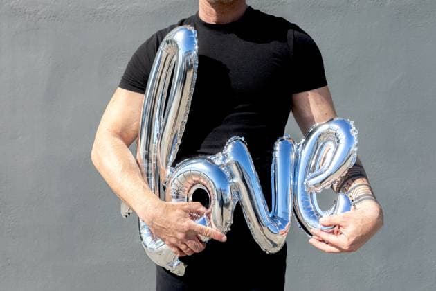 Creative Highlights Symbolbilder Cropped unrecognizable man in a black t-shirt holds shiny silver balloon letters spelling LOVE, symbolizing a romantic sentiment or celebration. Model Released SergioVictorVega_ID20495_605413_005 Copyright: xSergioxVictorxVegax RECORD DATE NOT STATED