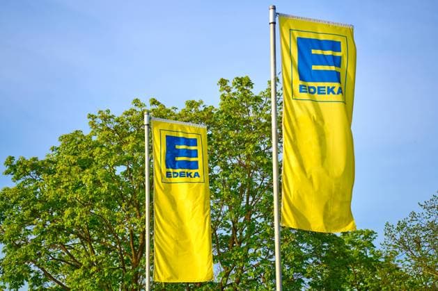 Augsburg, Bavaria, Germany - April 13, 2024: Flag of the German supermarket and food retailer EDEKA in front of green trees