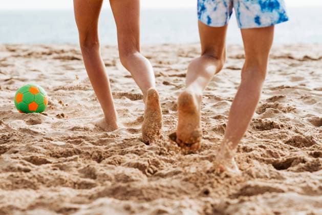 Siblings playing on beach with ball, playing football. Concept of family beach summer vacation with kids. Siblings playing on beach with ball, playing football. Concept of family beach summer vacation with kids. Close up on legs. model released
