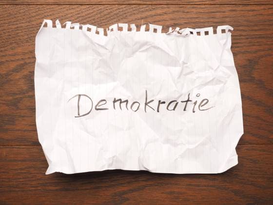 Wrinkled paper with the German word democracy on a wooden table