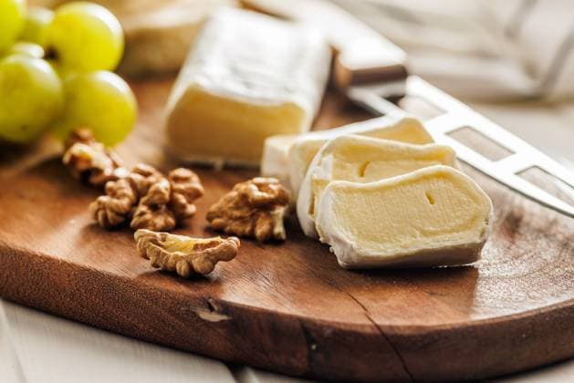 Sliced Brie cheese on a wooden board Artisan Brie cheese sliced on a round wooden cutting board, served with grapes and walnuts, ideal image for Gourmet cheese concepts Copyright: xZoonar.com JirixHERAx 21429469