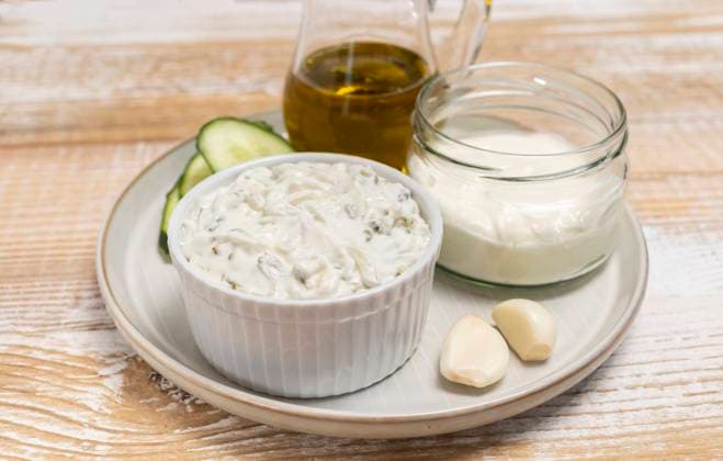 Traditional greek yogurt sauce Tzatziki,dressing in white bowl, made of grated cucumbers, sour cream yogurt,olive oil,garlic,herbs with ingredients on wooden table. Close up, horizontal Traditional greek yogurt sauce Tzatziki in white bowl, made of chopped cucumbers, sour cream yogurt,olive oil,garlic,herbs with ingredients on wooden table. Rustic style. Close up, horizontal plane. Copyright: x