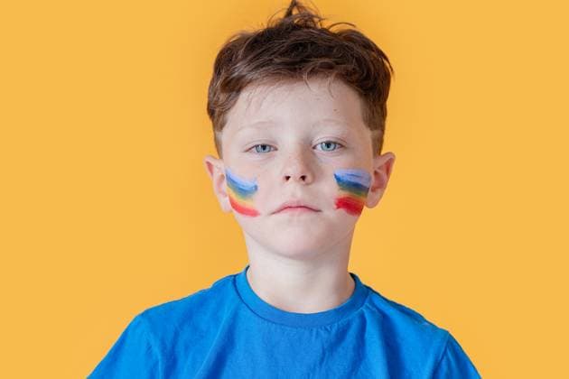 Creative Highlights Symbolbilder Portrait of a young boy with bold, colorful face paint standing against a vibrant yellow background, looking directly at the camera with a solemn expression Model Released HodeiUnzueta_ID21706_636719_031 Copyright: xHodeixUnzuetax