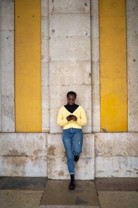 Creative Highlights Symbolbilder A young woman leans against a textured concrete wall with bright yellow accents, absorbed in texting on her smartphone, wearing a vivid yellow sweater and denim jeans Model Released OscarDeDios_ID21477_631658_008 Copyright: xOscarxDexDiosx