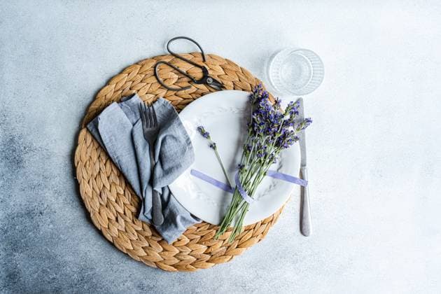 An inviting summer table setting featuring a woven placemat, white dinnerware, linen napkin, cutlery, a glass, and fresh lavender flowers Model Released AnnaBogush_ID21818_639754_004 Copyright: xAnnaxBogushx