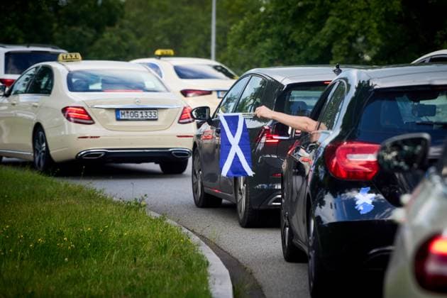 Munich, Bavaria, Germany - June 14, 2024: Motorcade in Munich for the European Championship 2024 or European Football Championship. Scottish fan holds a Scottish flag from the car, the vehicles are in a traffic jam with cabs at the Allianz Arena.