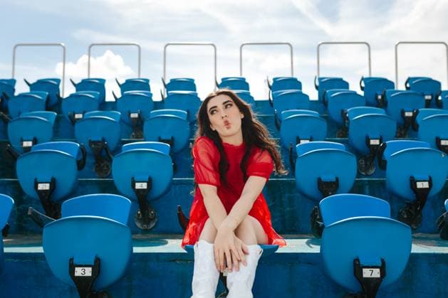 Creative Highlights Symbolbilder A young woman in red sits alone in a large blue stadium, playfully sending a kiss towards the camera under a bright sky Model Released CamilleGirard_ID21698_636456_024 Copyright: xCamillexGirardx