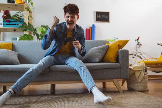 IMAGO Creative, Lifestyle, Gaming Cheerful man winning video game with controller at home model released, Symbolfoto property released, ALZF00282