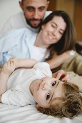 Creative Highlights Symbolbilder Cute baby son lying near parents on bed at home model released, Symbolfoto property released, EYAF03036