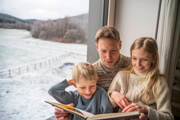 Father with children reading book by window at home in winter model released, Symbolfoto property released, NJAF01076