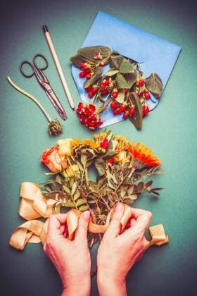 Female hand making autumn flowers arrangements on table workspace with scissors , envelope and ribbon, top view ,model released, Symbolfoto