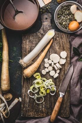 Healthy vegetables cooking and eating concept. Leek and parsnip root vegetables on cutting board with knife and pot with broth on dark rustic background, top view. ,model released, Symbolfoto