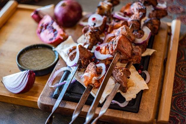 A rustic presentation of Georgian mtsvadi, showcasing succulent grilled meat skewers, served on a wooden board with sliced onions, pomegranate seeds, and traditional flat bread Perfect for culinary themes Model Released AnnaBogush_ID22661_660722_004 Copyright: xAnnaxBogushx