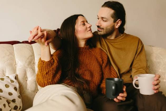 A Caucasian woman and man sitting closely on a cream-colored sofa, sharing a tender gaze. The woman, holding the man s hand, lovingly looks at him while he, with a subtle smile. They each hold a cup, adding a relaxed, homely vibe. Model Released CamilleGirard_ID21717_637084_022 Copyright: xCamillexGirardx