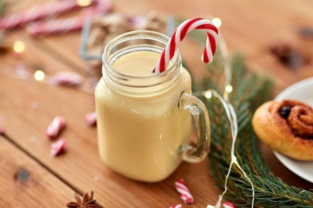 christmas and seasonal drinks concept - eggnog in glass mug with candy cane decoration, cinnamon buns, fir tree brunch and garland lights on wooden background. eggnog with candy cane in mug and cinnamon buns ,model released, Symbolfoto