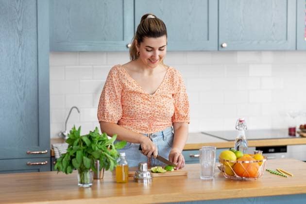 culinary and people concept - happy smiling young woman making cocktail drinks with lime and peppermint at home kitchen. woman making cocktail drinks at home kitchen ,model released, Symbolfoto