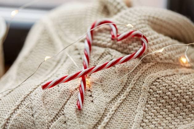 christmas, clothes and objects concept - close up of warm wool braided sweater, candy cane and electric garland string at home. close up of sweater, candy cane, christmas garland ,model released, Symbolfoto