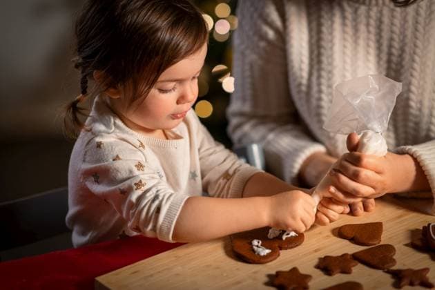 family, cooking and winter holidays concept - happy mother and baby daughter with icing in baking bag decorating gingerbread cookies at home on christmas. mother and daughter decorating gingerbread at home ,model released, Symbolfoto