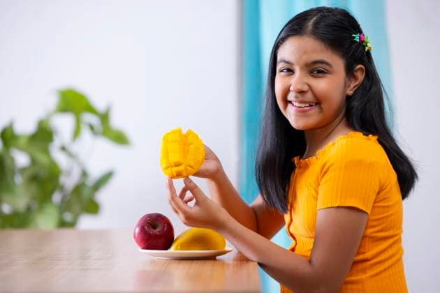 Portrait of cheerful girl holding a segmented slice of mango ,model released, Symbolfoto