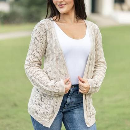 A Woman wearing a beige knitted cardigan over a white top and blue jeans in a park setting 25257753 ,model released, Symbolfoto RECORD DATE NOT STATED
