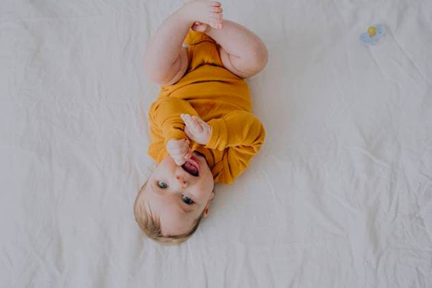 Creative Highlights Symbolfotos Cute baby boy in orange bodysuit lying on back in bed at home model released, Symbolfoto, AAZF01963