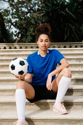 Female soccer player holding a soccer ball while sitting on stairs outdoors in Barcelona. model released, Symbolfoto, GDBF00144