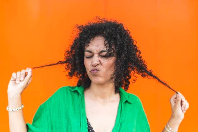 Creative Highlights Symbolfotos Woman with puckering face and eyes closed pulling hair in front of orange wall model released, Symbolfoto, JAQF01374