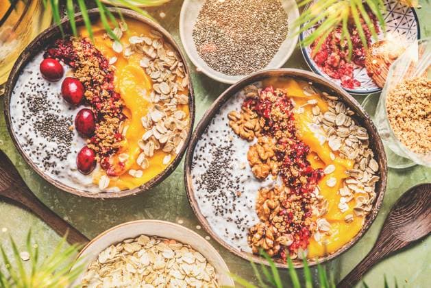 Smoothie mango bowls with chia seeds yogurt pudding and cranberries, nuts, oatmeal topping in coconut shells with spoon, top view. Healthy clean breakfast food ,model released, Symbolfoto