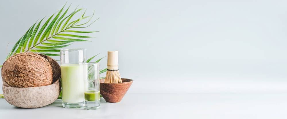 Matcha latte drink with coconut milk on table with whole coconut , matcha espresso and macha whisk, front view, banner. Healthy detox nutrition, vegan food and clean eating concept. Copy space, banner ,model released, Symbolfoto