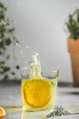 Homemade splashing orange lemonade in glass with thyme on kitchen table at wall and plant background. Refreshing drink with summer fruit. Front view. ,model released, Symbolfoto