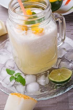 fresh vegetarian tropical melon cocktail with coconut milk and mango. served in transporant cup with ice, fresh melon, mango, lime, melissa and coconut milk on grey napkin. close up ,model released, Symbolfoto