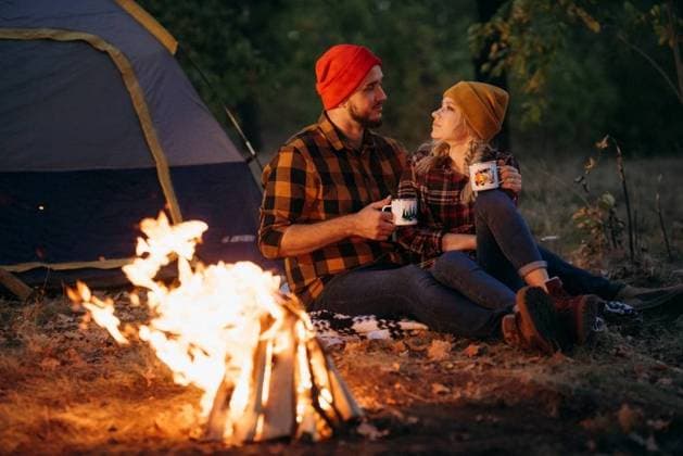 Young couple a guy and a girl in bright knitted hats stopped at a camping near the fire ,model released, Symbolfoto